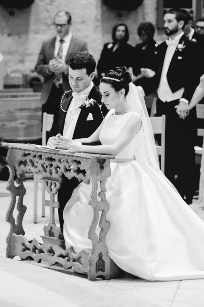 Bride and groom kneeling during wedding mass with rosary lasso wrapped around them