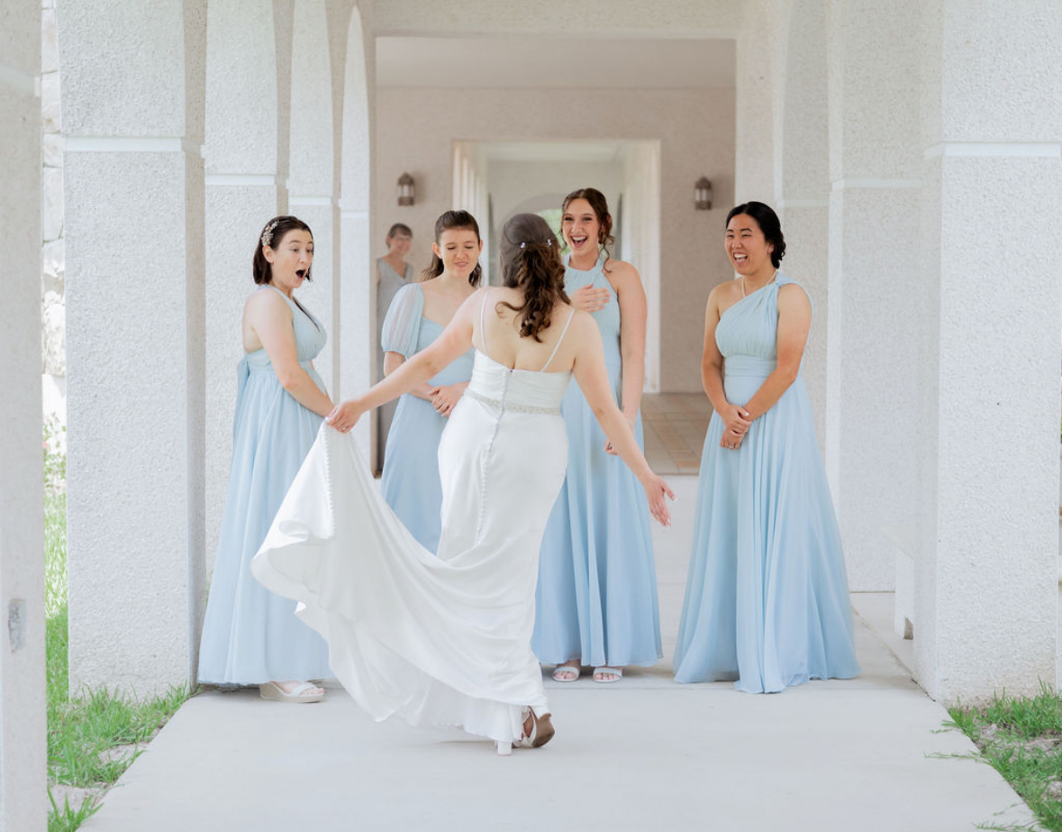 A group of bridesmaids smiling as they see the bride in her gown. 
